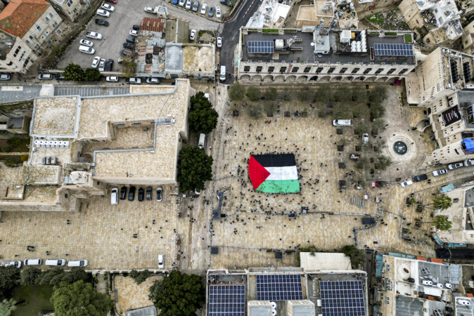 - Cette vue aérienne montre des fêtards déployant un drapeau palestinien géant alors qu'ils se rassemblent sur la place de la Crèche à l'extérieur de l'église de la Nativité dans la ville biblique de Bethléem en Cisjordanie occupée, la veille de Noël (selon la tradition occidentale), le 24 décembre 2023. (Photo HAZEM BADER / AFP)