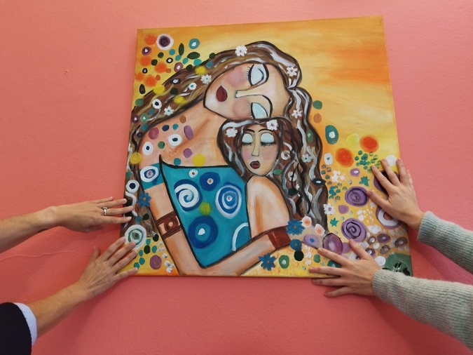 Deux des femmes qui ont témoigné entourent de leurs mains l'oeuvre peinte par Thaïs, une autre femme bénéficiaire de l'aide apportée par Women Safe and Children Corsica,.