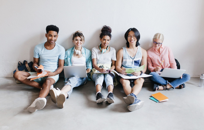 Portrait de jeunes gens avec des ordinateurs portables et des smartphones, assis ensemble sur le sol. Les étudiants écrivant des conférences tenant des manuels sur leurs genoux. (lookstudio)