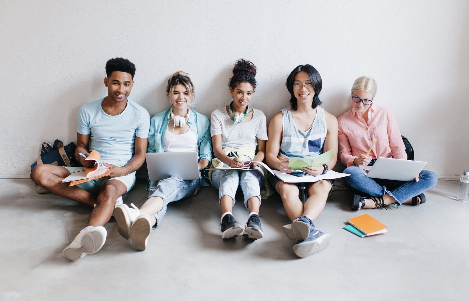 Portrait de jeunes gens avec des ordinateurs portables et des smartphones, assis ensemble sur le sol. Les étudiants écrivant des conférences tenant des manuels sur leurs genoux. (lookstudio)