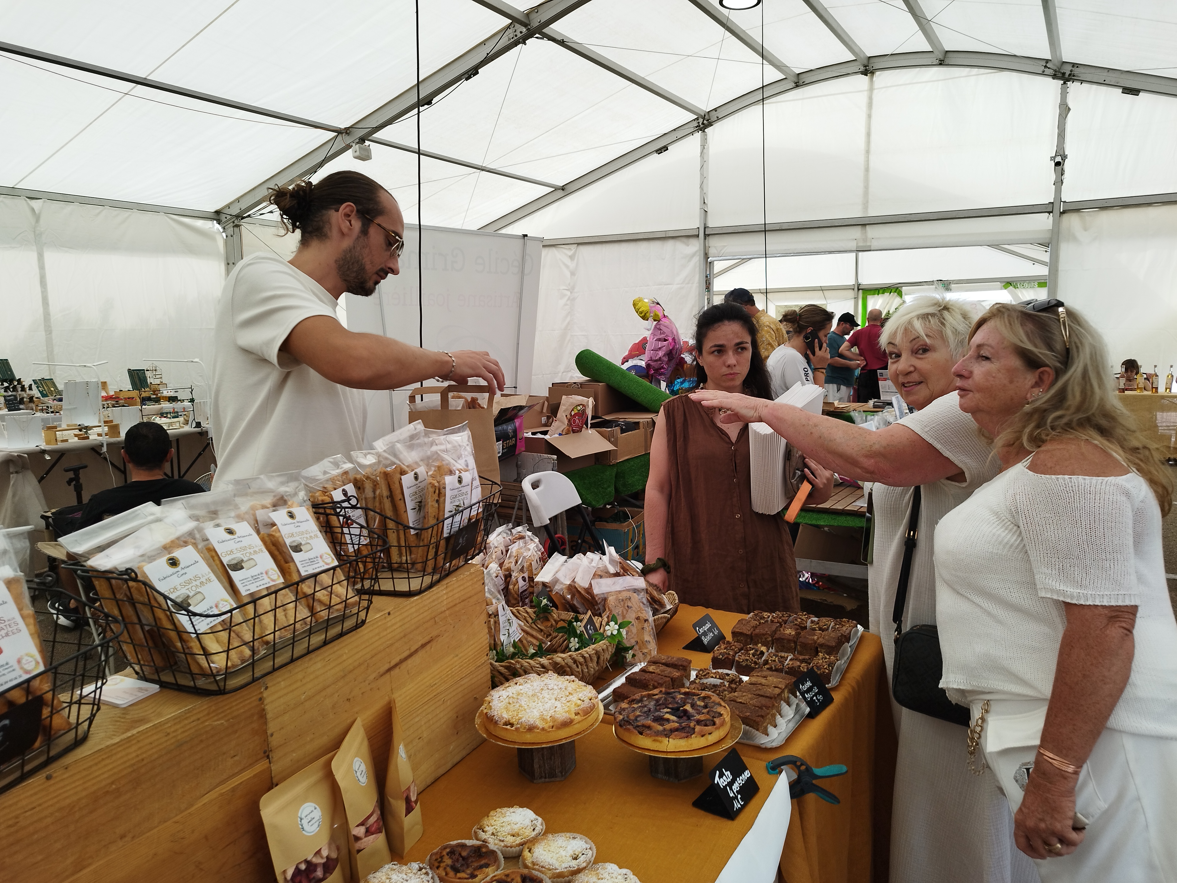 Elisabeth tend le bras pour récupérer les pâtisseries qu'elle vient d'acheter à Pauline (au centre), sa pâtissière favorite.